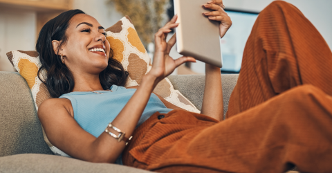 Vrouw ligt op de bank met een tablet in haar handen
